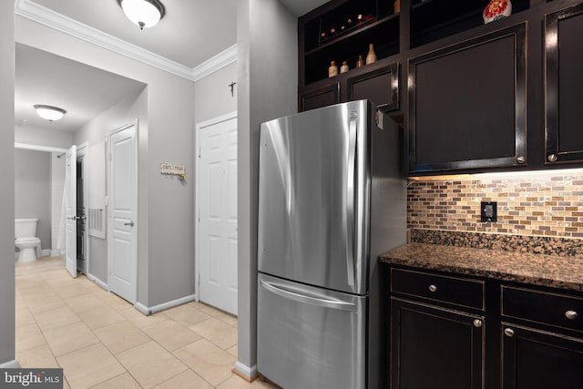 kitchen featuring crown molding, tasteful backsplash, light tile patterned floors, freestanding refrigerator, and dark stone countertops