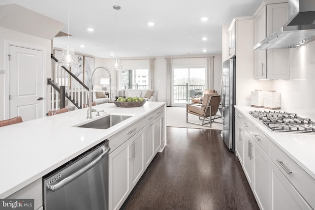 kitchen with appliances with stainless steel finishes, a sink, light countertops, open floor plan, and wall chimney exhaust hood