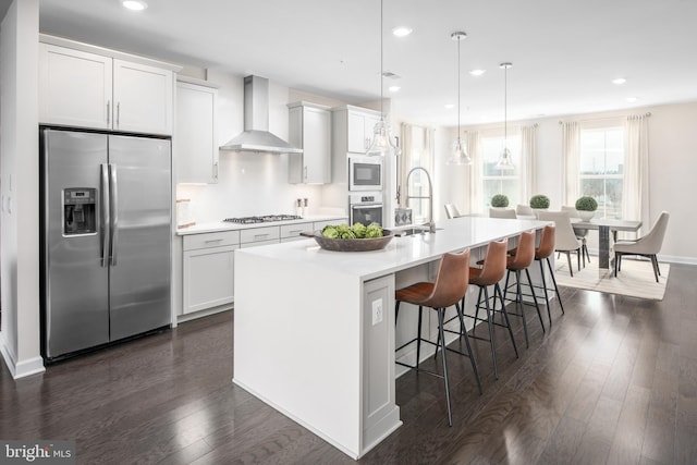 kitchen featuring wall chimney range hood, a sink, light countertops, stainless steel appliances, and a spacious island