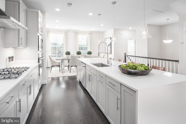 kitchen featuring a kitchen island with sink, visible vents, appliances with stainless steel finishes, a sink, and wall chimney exhaust hood