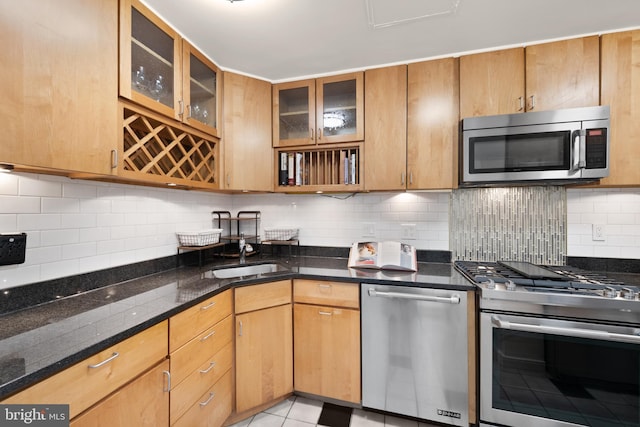 kitchen featuring stainless steel appliances, tasteful backsplash, dark stone countertops, and a sink