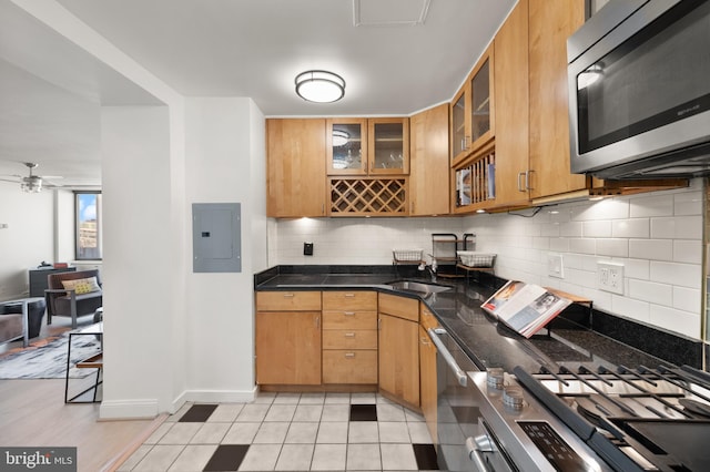 kitchen with appliances with stainless steel finishes, electric panel, ceiling fan, tasteful backsplash, and glass insert cabinets