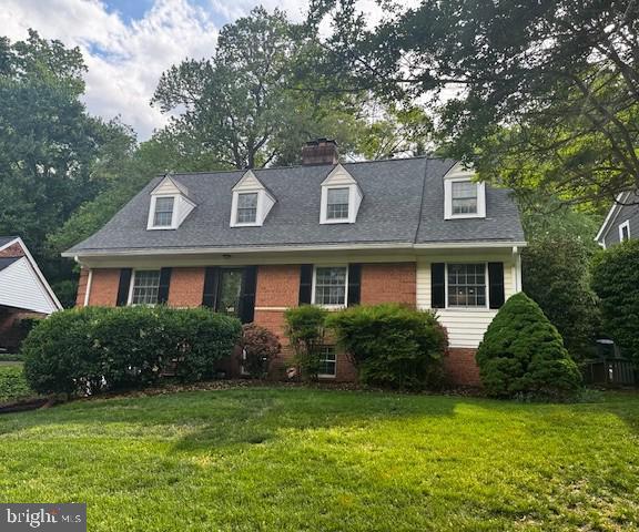 new england style home with brick siding, a shingled roof, a chimney, and a front yard