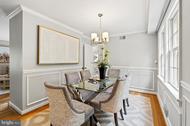 708 W Timber Branch Pkwy, Alexandria, VA 22302 - dining room featuring light wood finished floors, a chandelier, ornamental molding, a decorative wall, and wainscoting