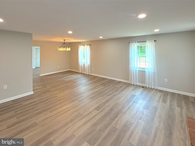 empty room featuring an inviting chandelier, wood finished floors, baseboards, and recessed lighting