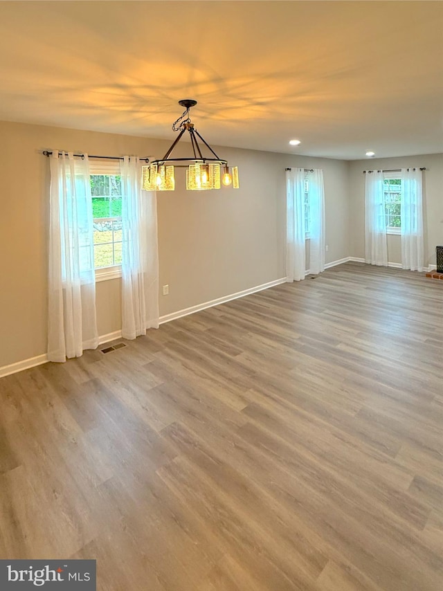 empty room featuring an inviting chandelier, wood finished floors, visible vents, baseboards, and recessed lighting