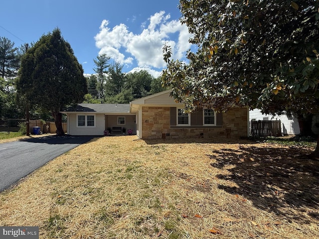 view of front of home with stone siding, aphalt driveway, a front lawn, and fence