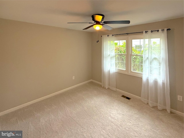 unfurnished room featuring light colored carpet, visible vents, baseboards, and a ceiling fan