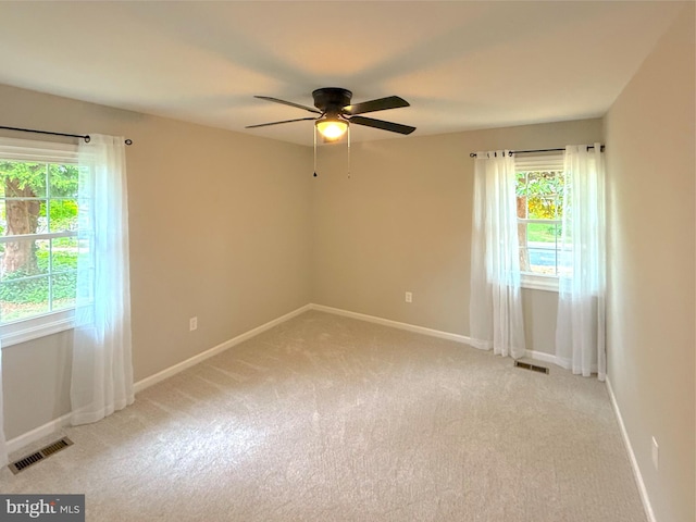 empty room with ceiling fan, light carpet, visible vents, and plenty of natural light