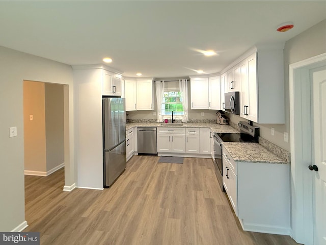kitchen with light stone countertops, recessed lighting, light wood finished floors, a sink, and stainless steel appliances