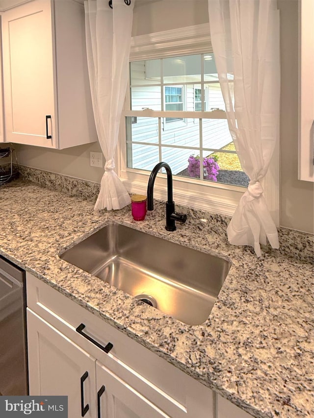 kitchen featuring white cabinets, dishwasher, light stone counters, and a sink