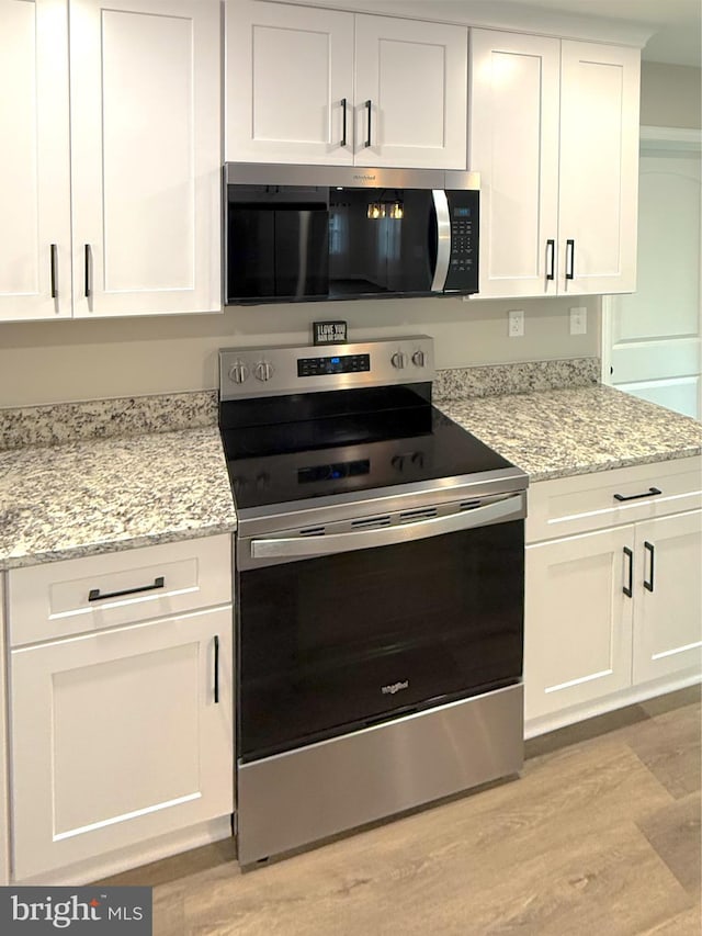 kitchen with white cabinets, appliances with stainless steel finishes, light stone counters, and light wood-style flooring