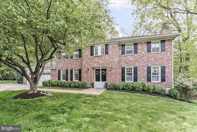 colonial home featuring french doors, brick siding, a chimney, and a front yard