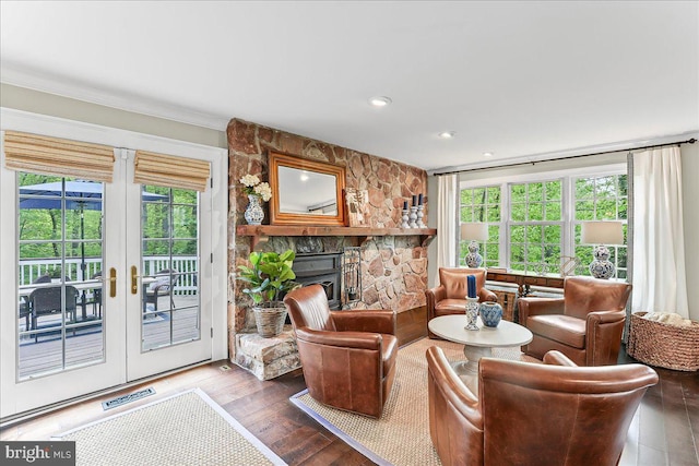 living area with a stone fireplace, wood-type flooring, a healthy amount of sunlight, and visible vents