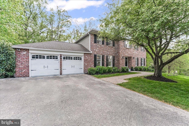 colonial house with a garage, a front yard, driveway, and brick siding