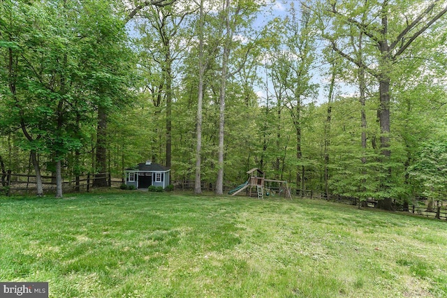 view of yard with a playground, fence, an outbuilding, and a forest view