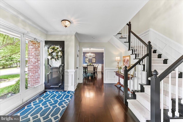 entryway with stairs, a notable chandelier, a decorative wall, and dark wood-style floors