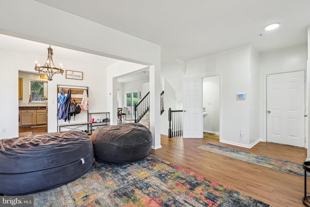 living room featuring wood finished floors, a chandelier, baseboards, and stairs