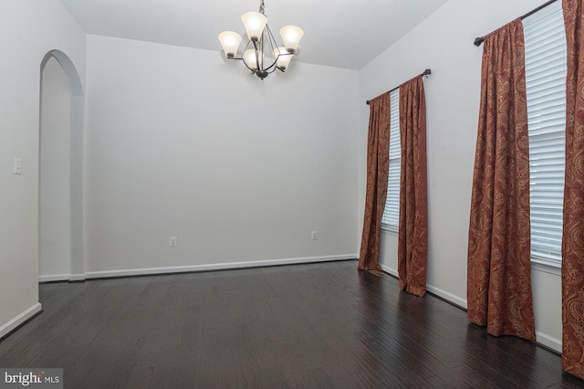 spare room featuring wood finished floors, a chandelier, baseboards, and arched walkways