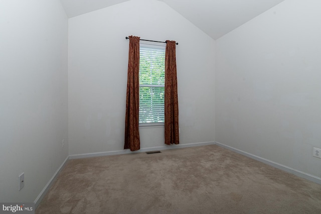 carpeted spare room featuring vaulted ceiling and baseboards