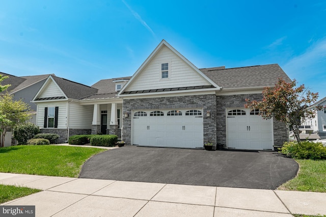 craftsman house featuring a standing seam roof, an attached garage, stone siding, aphalt driveway, and a front lawn