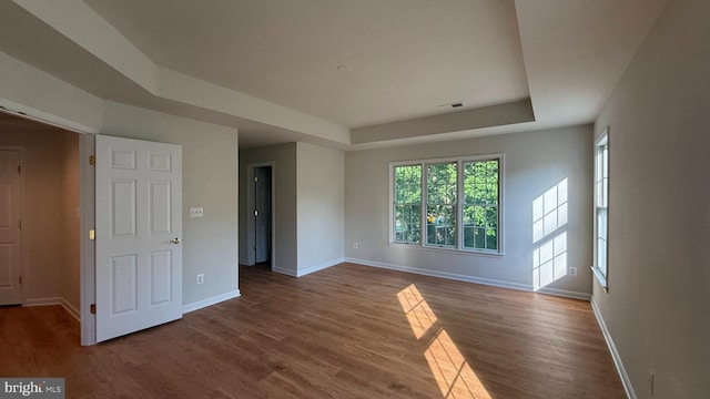 empty room featuring a tray ceiling, baseboards, and wood finished floors