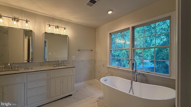 bathroom with marble finish floors, a freestanding bath, tile walls, double vanity, and a wainscoted wall