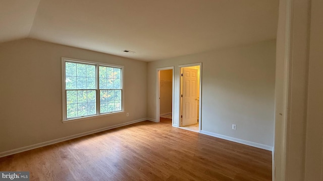 unfurnished bedroom with light wood finished floors, baseboards, vaulted ceiling, and a spacious closet