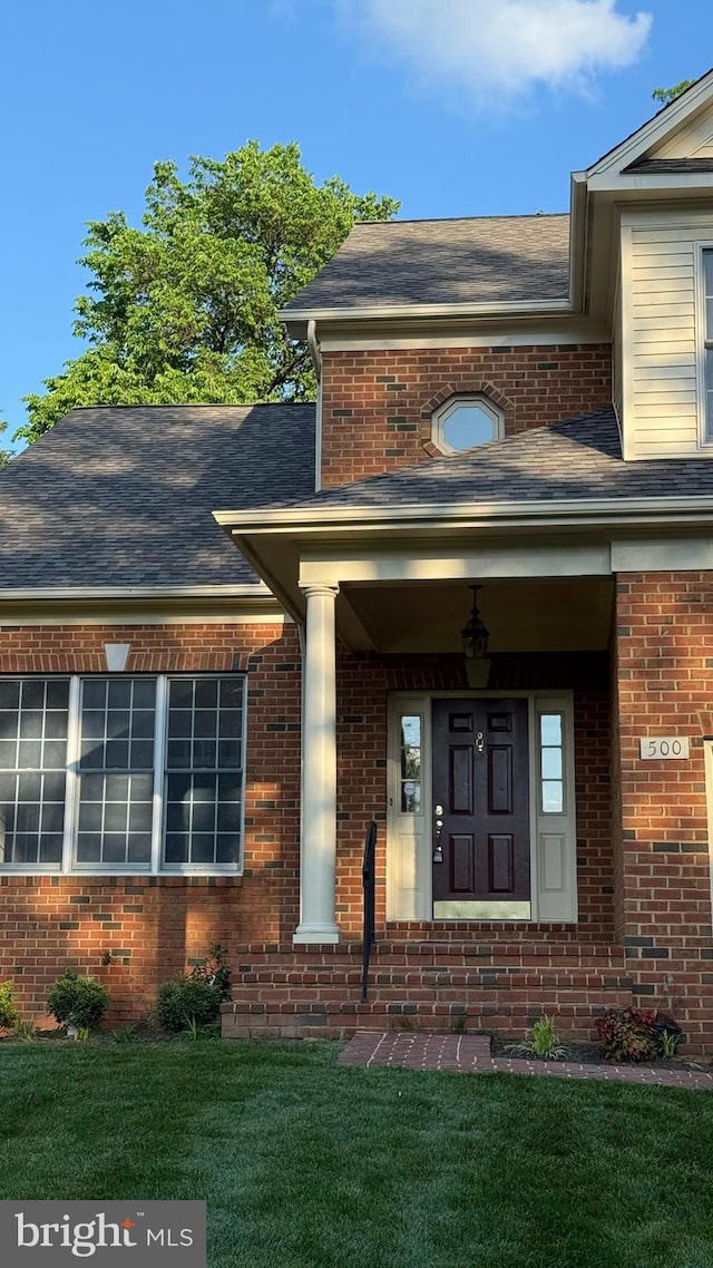 entrance to property with brick siding, a yard, and a shingled roof
