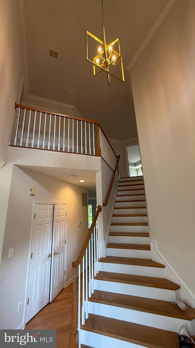 stairs with a high ceiling, a chandelier, and wood finished floors