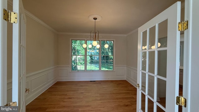 unfurnished dining area featuring wood finished floors, wainscoting, ornamental molding, and a decorative wall