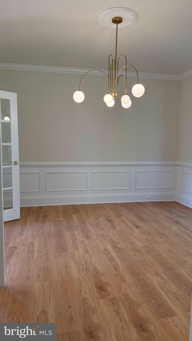 unfurnished room with crown molding, a decorative wall, wainscoting, and wood finished floors