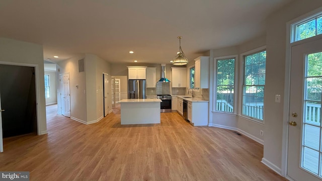 kitchen featuring stainless steel appliances, wall chimney exhaust hood, a sink, white cabinetry, and a kitchen island