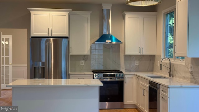 kitchen with stainless steel appliances, a sink, wall chimney exhaust hood, tasteful backsplash, and white cabinets