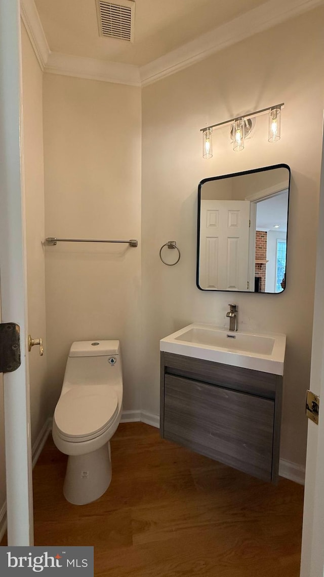 bathroom featuring wood finished floors, ornamental molding, vanity, toilet, and baseboards