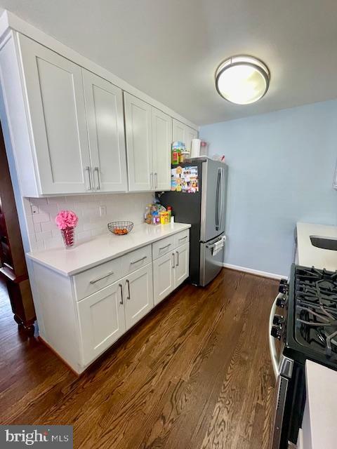 kitchen featuring white cabinets, light countertops, stainless steel appliances, dark wood-type flooring, and backsplash