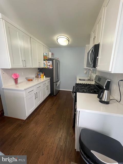 kitchen with appliances with stainless steel finishes, a sink, white cabinetry, decorative backsplash, and dark wood-style floors