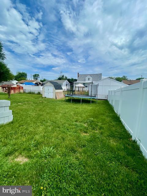 view of yard featuring a fenced backyard, a trampoline, an outbuilding, and a shed