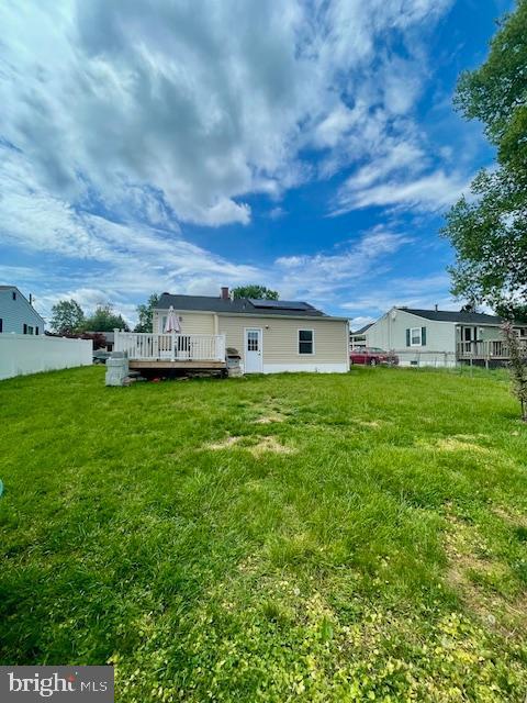 back of property featuring fence, a yard, a deck, and solar panels