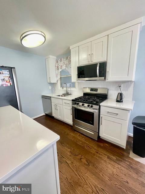 kitchen featuring appliances with stainless steel finishes, dark wood finished floors, a sink, light countertops, and white cabinetry