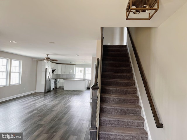 staircase with baseboards, ceiling fan with notable chandelier, and wood finished floors