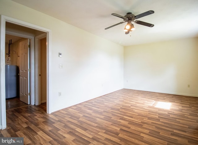 empty room with a ceiling fan, wood finished floors, water heater, and baseboards