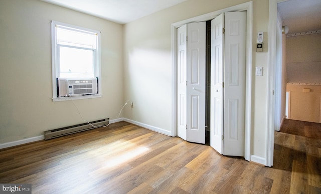 unfurnished bedroom featuring baseboard heating, cooling unit, wood finished floors, a closet, and baseboards