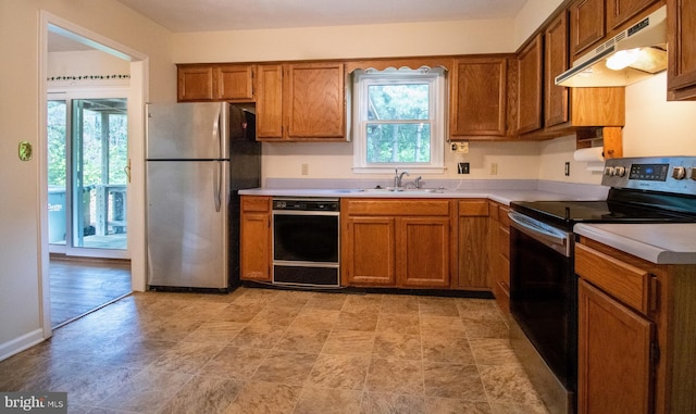 kitchen with under cabinet range hood, stainless steel appliances, a sink, brown cabinets, and light countertops