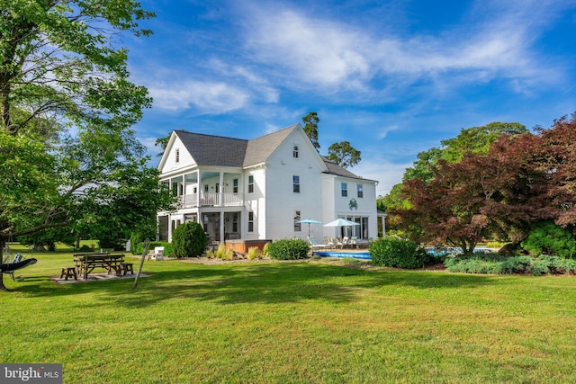 back of property featuring a shingled roof, an outdoor pool, a yard, and a balcony