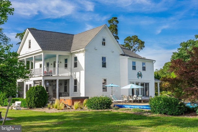 back of property with a hot tub, a lawn, a balcony, and roof with shingles