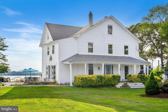 view of front of house with a shingled roof, covered porch, a chimney, and a front yard