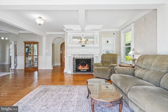living room featuring arched walkways, wallpapered walls, ornamental molding, and wood finished floors