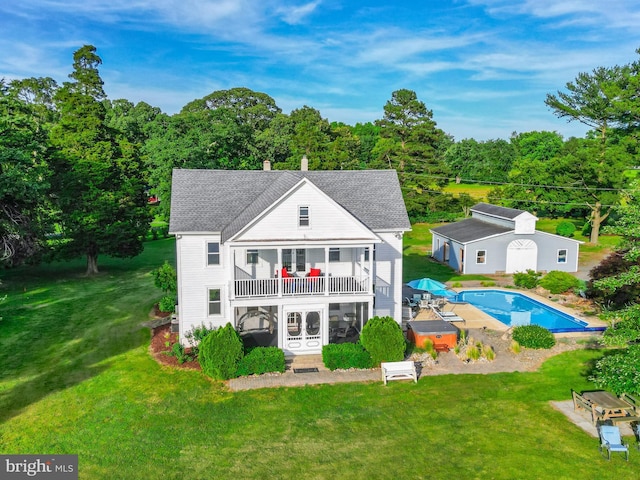 rear view of house featuring a lawn, roof with shingles, an outdoor pool, and a balcony