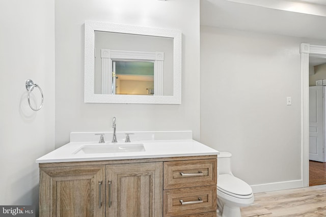 bathroom featuring toilet, baseboards, wood finished floors, and vanity